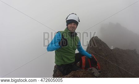 Young Male Climber Sitting On The Summit Of Ruminahui Volcano Wearing Green Coat And Helmet On A Clo