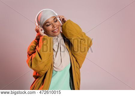 Overjoyed Multiracial Woman In Bomber Jacket And Hijab Listening Music In Wireless Headphones On Pin
