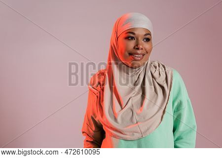 Carefree Multiracial Muslim Woman In Traditional Hijab Looking Away Isolated On Pinkish Grey