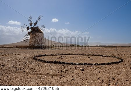 Old Traditional Windmill, Located In A Stone Desert. Blue Sky With Some White Clouds In The Winter. 