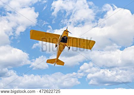 Yellow Single-engine Ultralight Airplane Flying In The Blue Sky With White Clouds