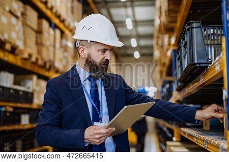 Manager In Suit Controlling Goods In A Waehouse.