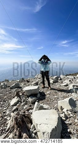 Asian Man Standing On Top Of A Nearby Mountain Looking At Mount Sindoro. West Java, Indonesia, March