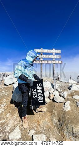 Asian Man Sitting On Top Of A Nearby Mountain Looking At Mount Sindoro. West Java, Indonesia, March