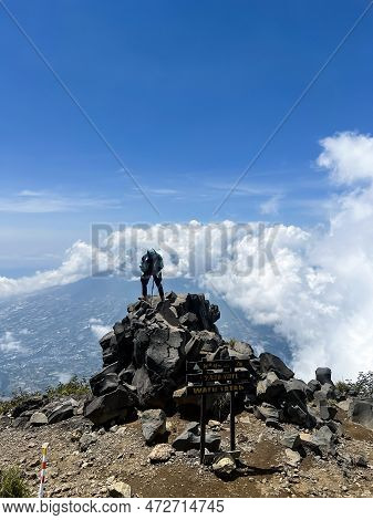 Asian Man Standing On Top Of A Nearby Mountain Looking At Mount Sindoro. West Java, Indonesia, March