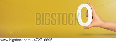 Numeral Zero In Hand. A Hand Holds A White Number Zero On A Yellow Background With Copy Space. Zero 
