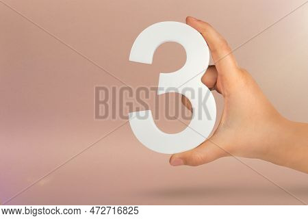 Number Three In Hand. Hand Holding White Number 3 On Red Background With Copy Space. Concept With Nu