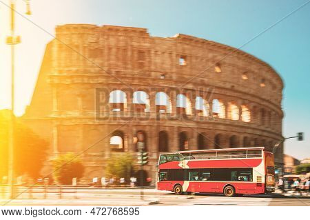 Rome, Italy. Colosseum. Glare Light On Red Hop On Hop Off Touristic Bus For Sightseeing Near Flavian