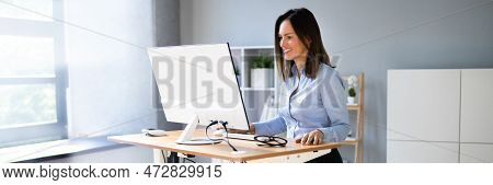 Woman Using Adjustable Height Standing Desk In Office For Good Posture
