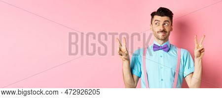 Funny Young Guy In Bow-tie, Entertain People On Holiday Event, Showing Peace Signs And Looking Aside