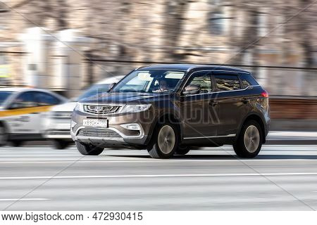 Fast Moving Geely Atlas On The City Road. Brown Suv Front Side View. Chinese Auto In Fast Motion Wit