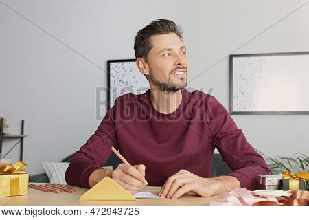 Man Writing Message In Greeting Card At Wooden Table In Room