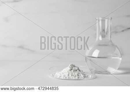 Petri Dish With Calcium Carbonate Powder And Laboratory Flask On White Table. Space For Text