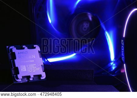 Close-up Of An Amd Ryzen 9 7900X Processor, Against The Backdrop Of Coolers With Light.