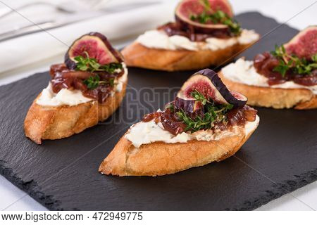 Canape Or Crostini With Toasted Baguette, Cream Cheese, Onion Jam, Figs And Fresh Thyme On A Slate B