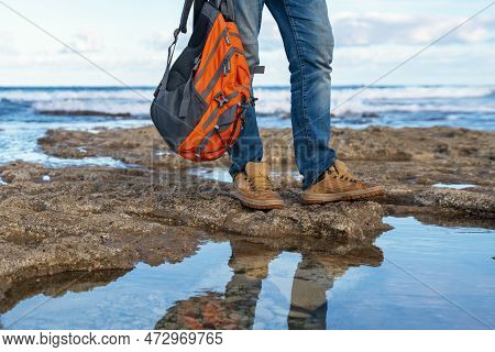 Man In Jeans With Orange Backback Relaxing Alone On The Seaside On Hot Sunny Day At Sunset. Travel  