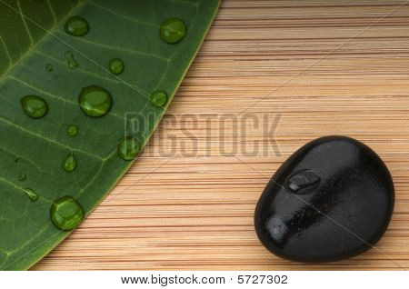 Folha verde e pedra preta com as gotas de chuva sobre o fundo de bambu