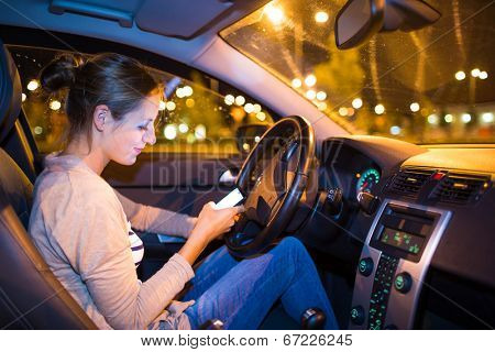 Pretty young woman using her smart phone while driving her car at night