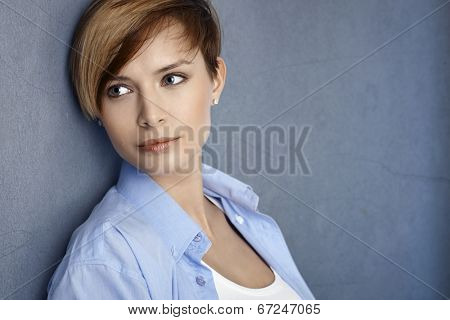 Closeup portrait of attractive young woman leaning to grey wall, smiling