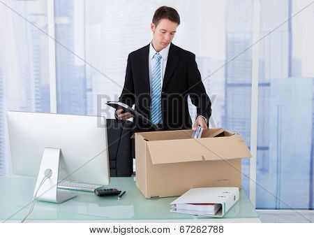 Businessman Collecting Office Supply In Cardboard Box At Desk