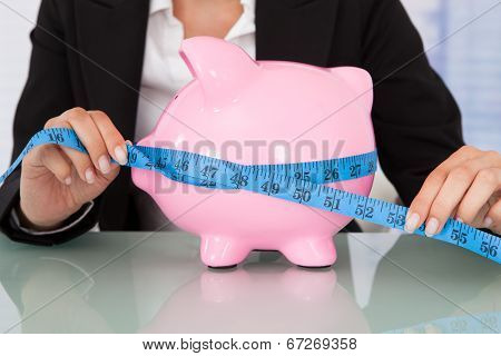 Businesswoman Measuring Piggybank At Desk