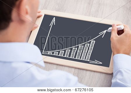 Businessman Drawing Bargraph On Slate At Desk
