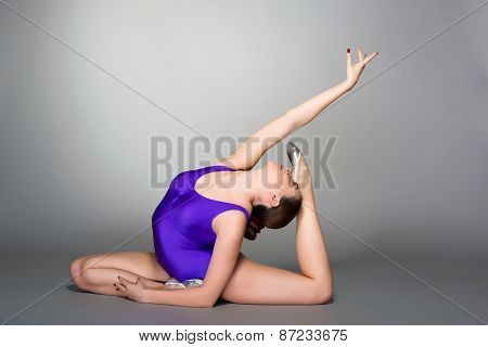 Young Female Contortionist In Purple Leotard On Dark Background