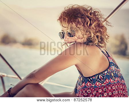 Portrait of beautiful happy woman with stylish hairdo having fun on sailboat, enjoying mild sunset light, funky style, active summer vacation
