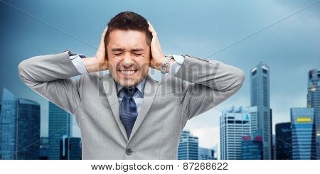 business, people, crisis and emotional pressure concept - businessman in suit covering his ears by hands over city background