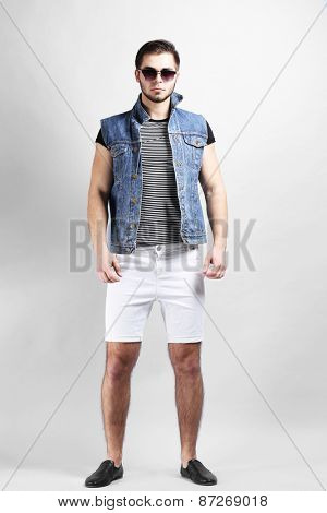 Man in white shorts and jeans vest on gray background