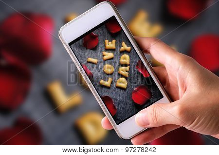 using mobile phone to take photos of Cookies ABC in the form of word I LOVE DADY alphabet with red r
