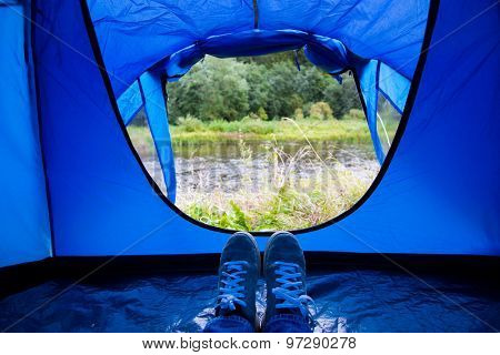 camping, travel, tourism, hike and people concept - close up of camper legs lying near blur tent entrance and enjoying natural landscape