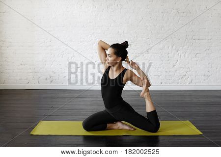 Sporty asian young woman doing yoga practice at green yoga mat in training class in the morning. Portrait of an exercise-focused asian female practicing stretching looking aside. Yoga concept