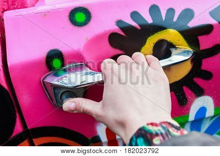 Female hand holding silver doorhandle of bright colorful car at festival