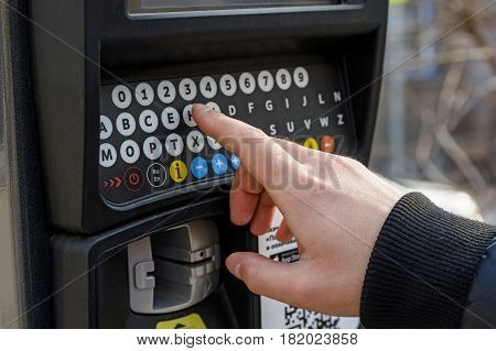 Close up of male hand pressing buttons on parking meter with colorful buttons in the street