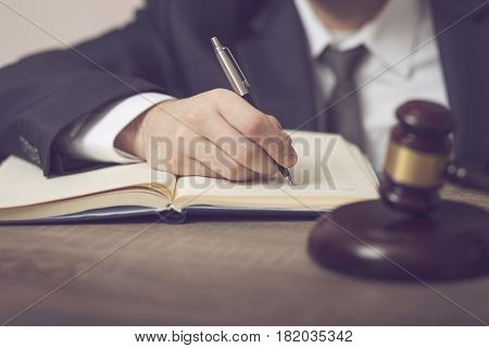 Detail of a judge sitting at his desk studying new laws and legislation and taking notes. Selective focus