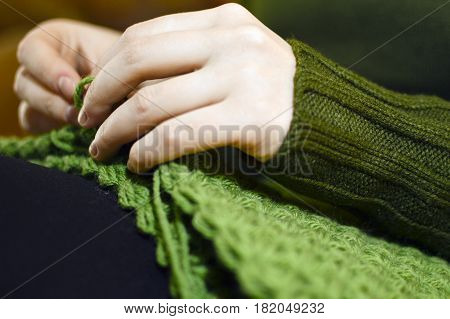 Women's hands knitting green scarf by needles