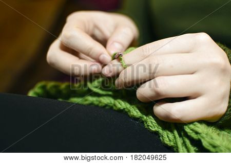 Women's hands knitting green scarf by needles