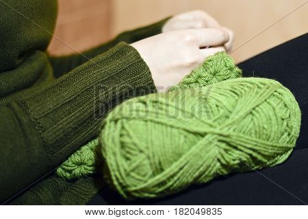 Women's hands knitting green scarf by needles