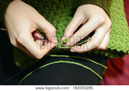 Women's hands knitting green scarf by needles