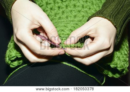 Women's hands knitting green scarf by needles