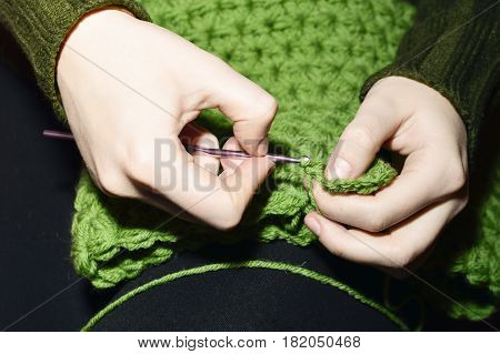 Women's hands knitting green scarf by needles