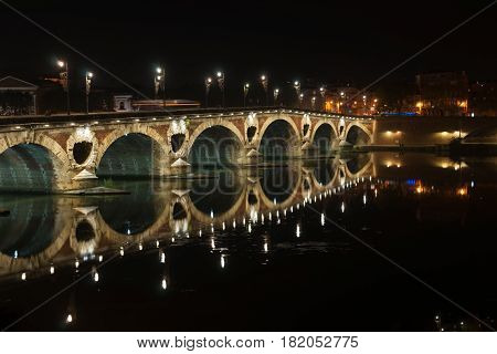 Pont Neuf beautifully illuminated on dark night across Garrone River Toulouse France.