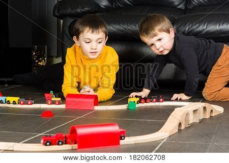 Children playing with wooden toy train. Brothers build wooden railroad at home.