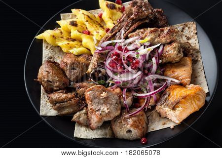 Lyulya kebab shish kebab grilled salmon fish onion and pomegranate grains on black plate. Close up image with selective focus.