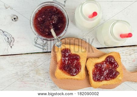 Toasts with strawberry jam and milk for breakfast on white rusric wooden background. Top view.