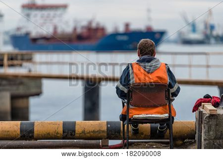 Maritime transportation industry. Roustabout leisure time sits on the embankment and looking at ships.