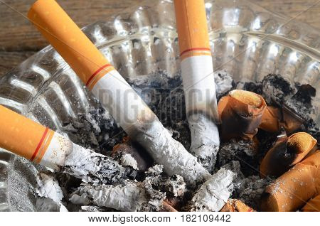 A close up image of lit cigarettes in a dirty ashtray.