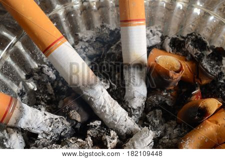A close up image of lit cigarettes in a dirty ashtray.