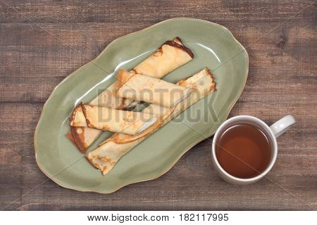 Delicious cheese blintz on green plate and cup of tea on wooden vintage tray
